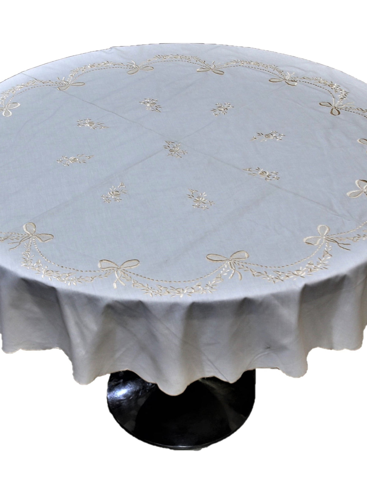 Round ivory table cover with a cream embroidered bow-and-garland pattern and a scalloped edge