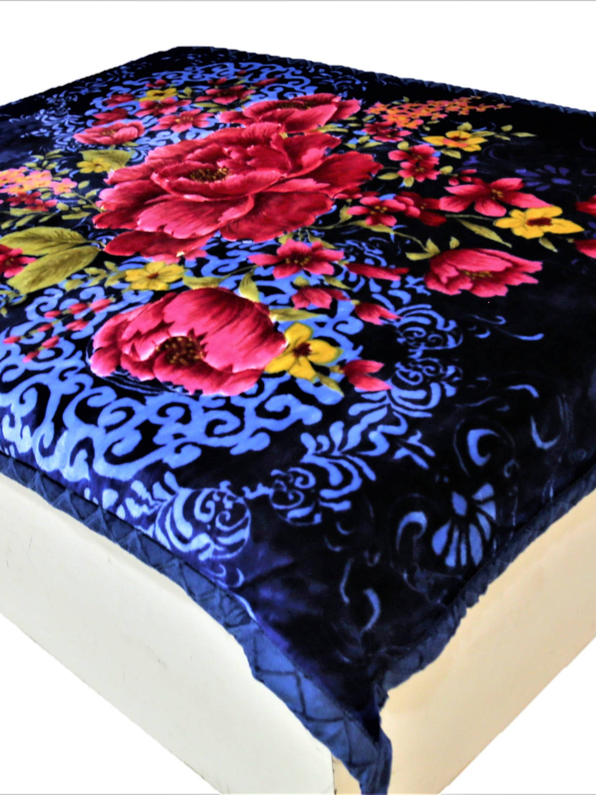 Navy-blue velour blanket with a large red-pink peony floral print and pale-blue scroll damask pattern, spread over a bed