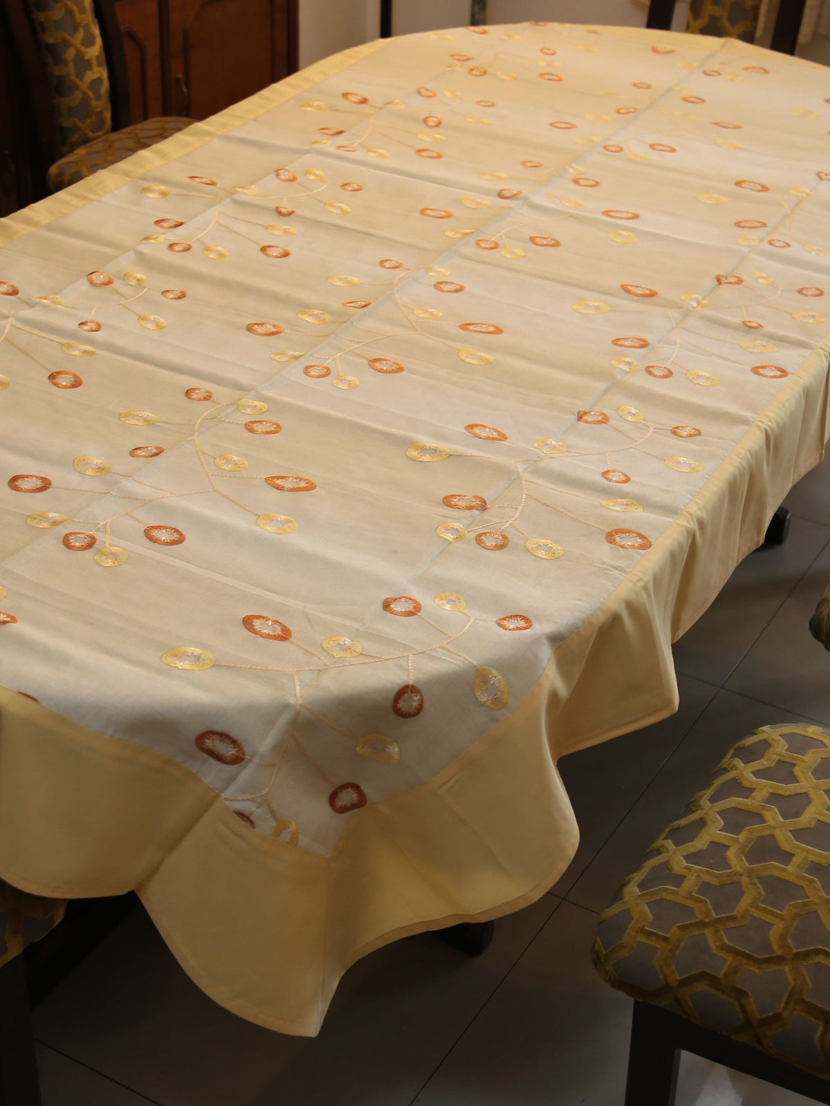 Cream oval table cover with a rust-orange and gold ring embroidery vine pattern and a solid cream border
