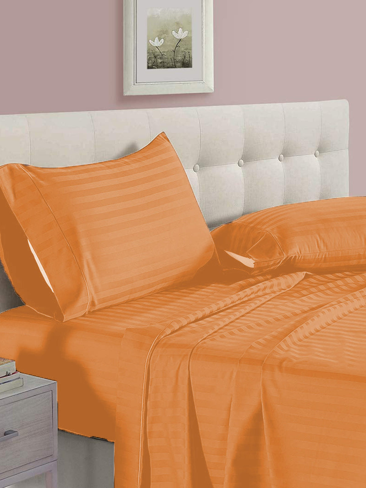 Solid orange satin-stripe cotton bedsheet with matching pillow covers on a tufted cream headboard bed