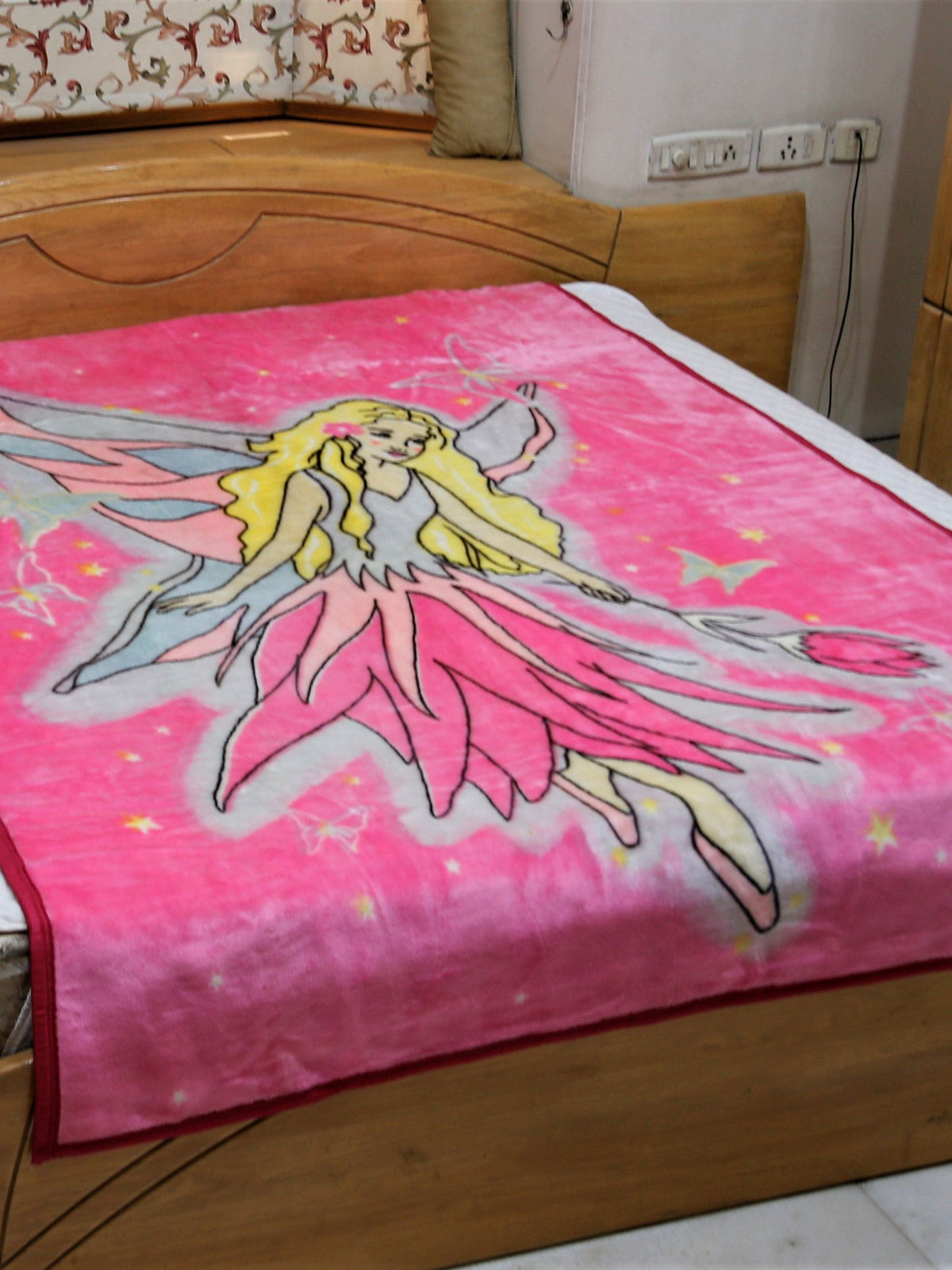 Hot-pink blanket with a printed fairy angel illustration in a flowing pink dress with wings, stars, and butterflies, spread on a bed