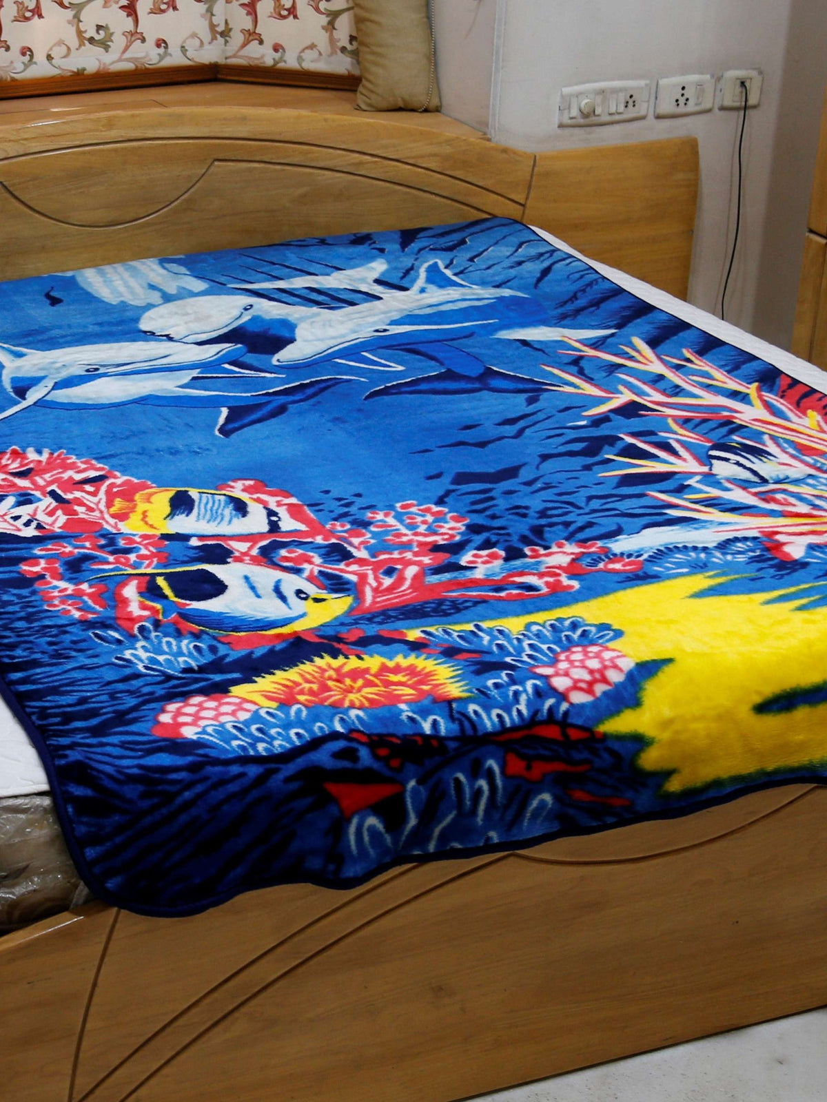 Royal-blue blanket with a printed underwater scene of dolphins, coral reef, and tropical fish, draped over a bed