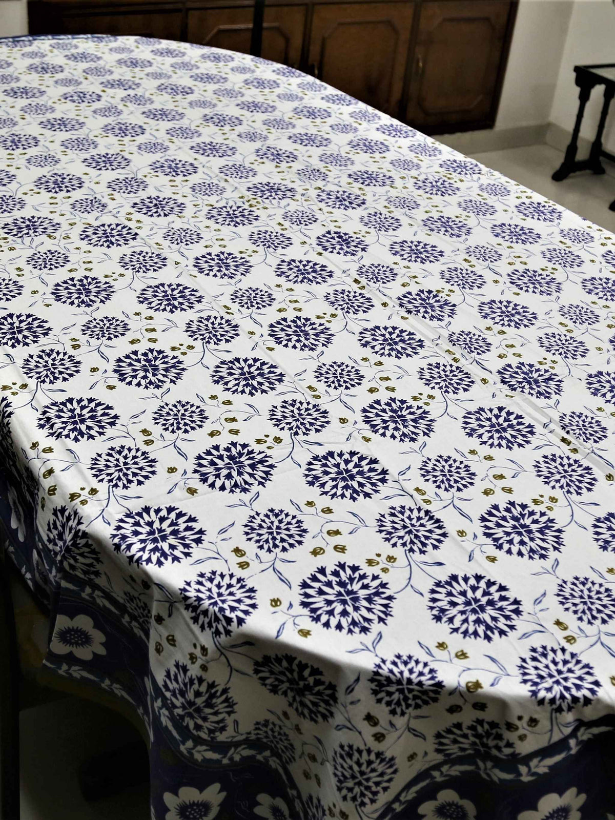 White oval table cover with a navy-blue dahlia and pompom floral print and a navy border with white flowers