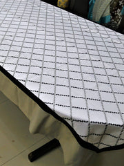 White table cover with a black and grey diamond-lattice embroidered pattern and a plain beige-tan underskirt with a black edge trim