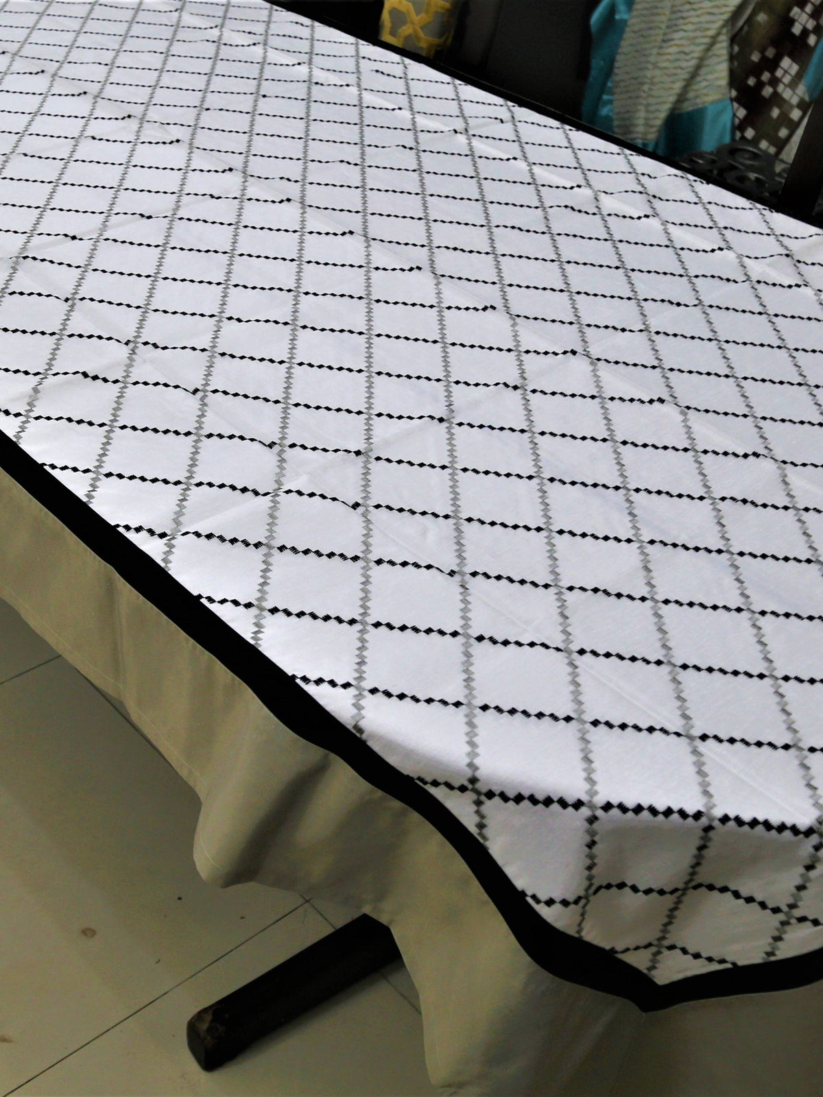 White table cover with a black and grey diamond-lattice embroidered pattern and a plain beige-tan underskirt with a black edge trim
