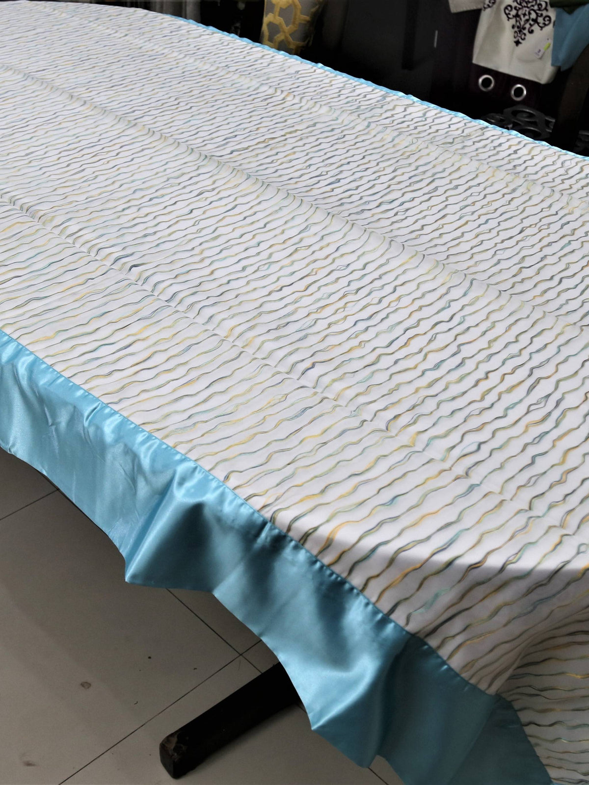 Cream table cover with a wavy multicolour stitch-line pattern and a solid sky-blue satin border