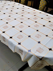 White-ivory table cover with a geometric cutwork square pattern and brown scroll motifs inside each square