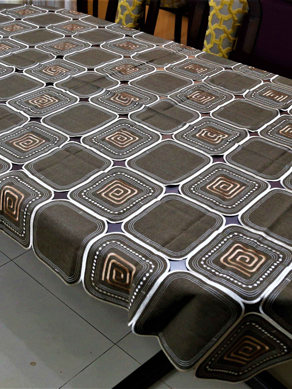 Brown table cover with a cutwork square pattern and copper spiral motifs inside each square