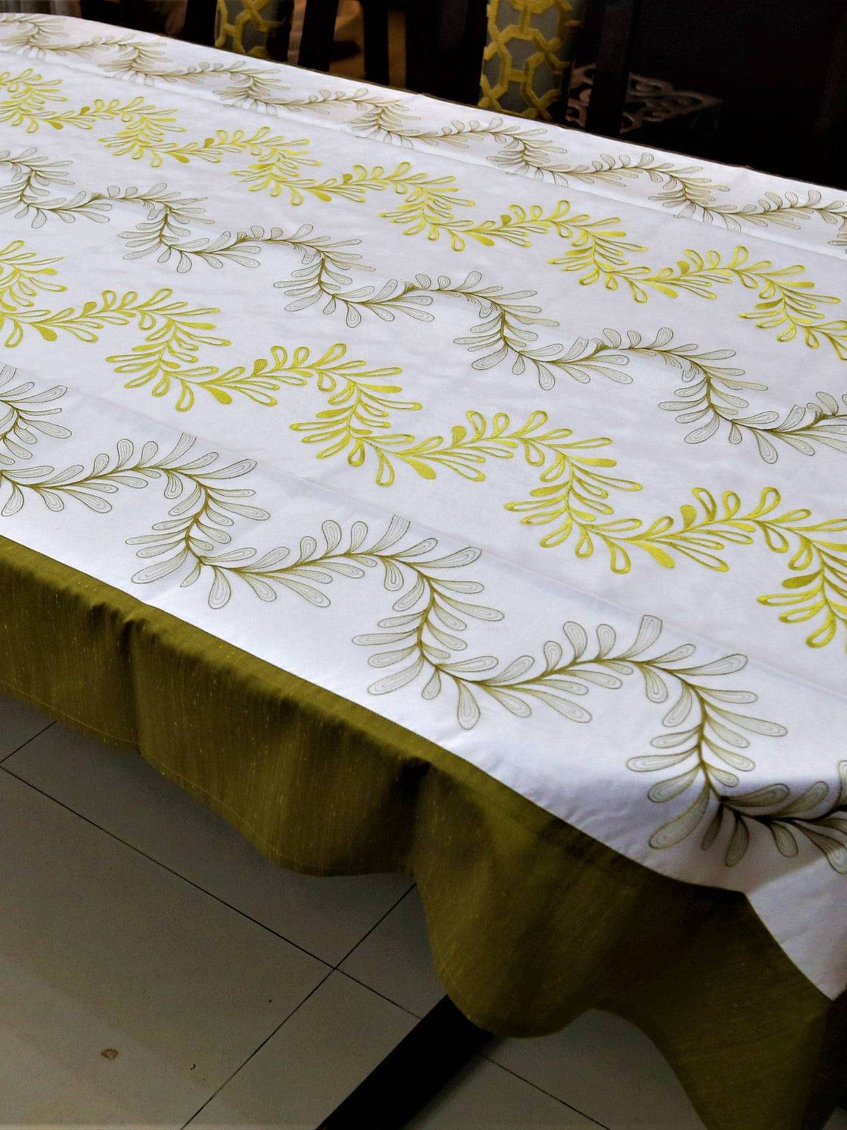 White table cover with a green and yellow embroidered fern-leaf vine pattern and a solid olive-green underskirt
