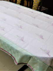 White table cover with lavender embroidered wheat-sprig motifs and scattered gold dots, with a mint-green checkered underskirt trimmed in pink