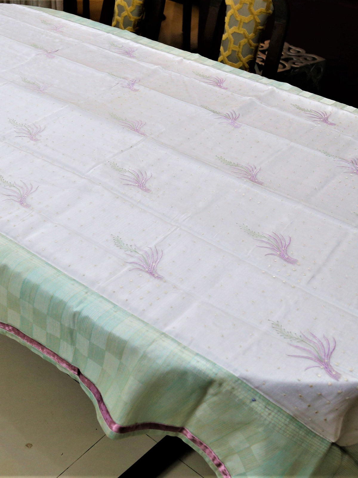White table cover with lavender embroidered wheat-sprig motifs and scattered gold dots, with a mint-green checkered underskirt trimmed in pink