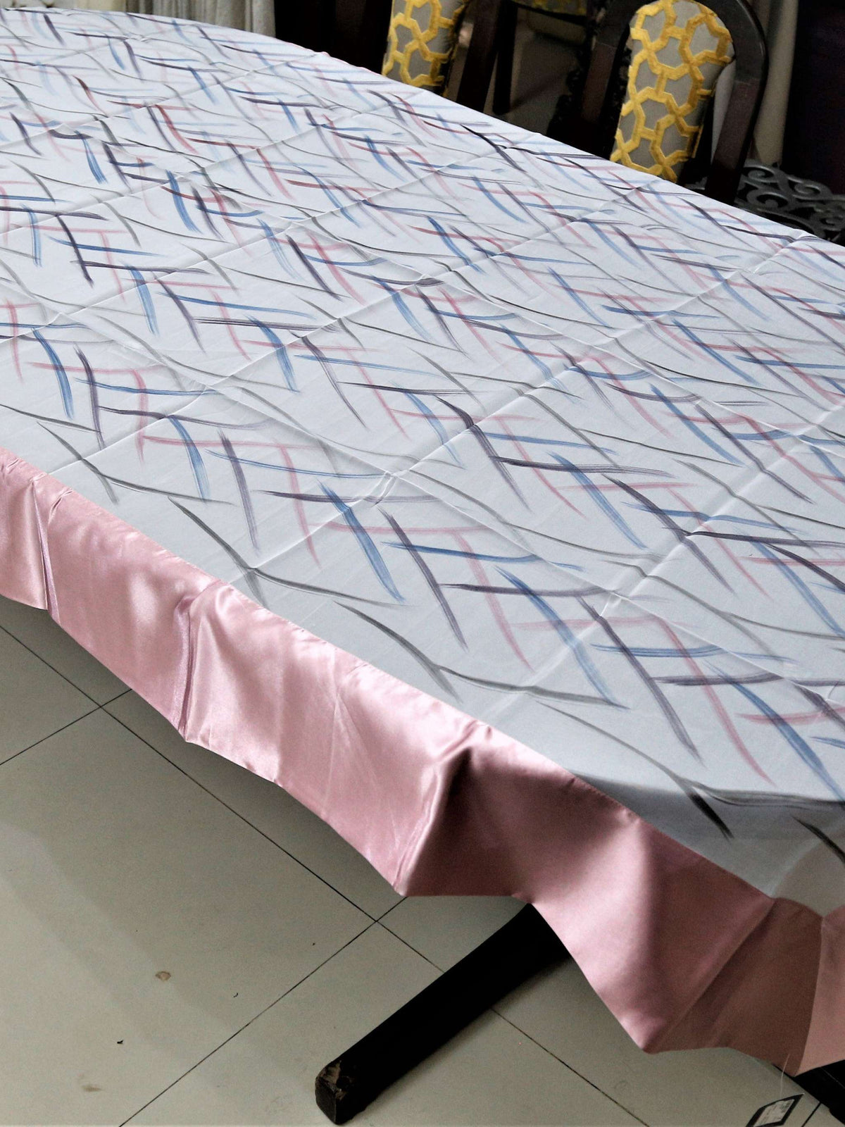 White table cover with a criss-crossing blue, pink, and grey stitch-line pattern and a solid blush-pink satin border