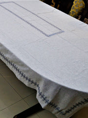 Light grey linen table cover with a navy embroidered scallop-chain border pattern