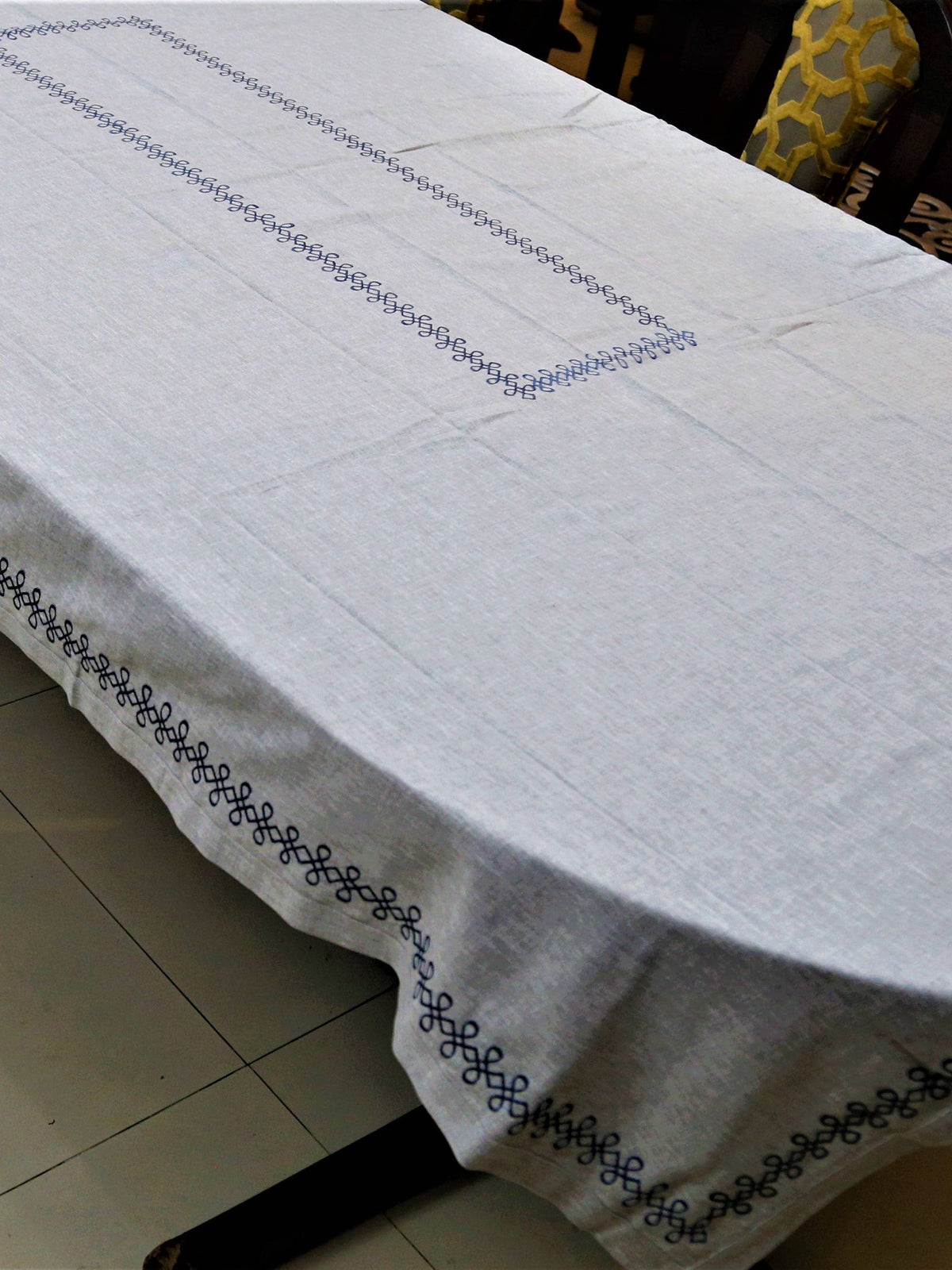 Light grey linen table cover with a navy embroidered scallop-chain border pattern