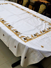White table cover with a gold-brown embroidered paisley-and-vine corner border and scattered small leaf motifs