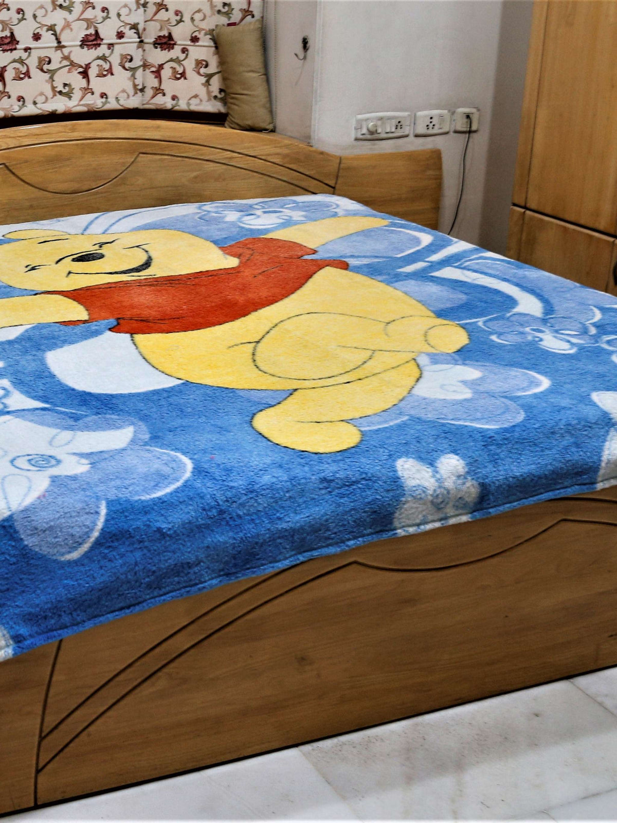 Blue plush blanket with a printed Winnie the Pooh design and white flowers, draped over a bed