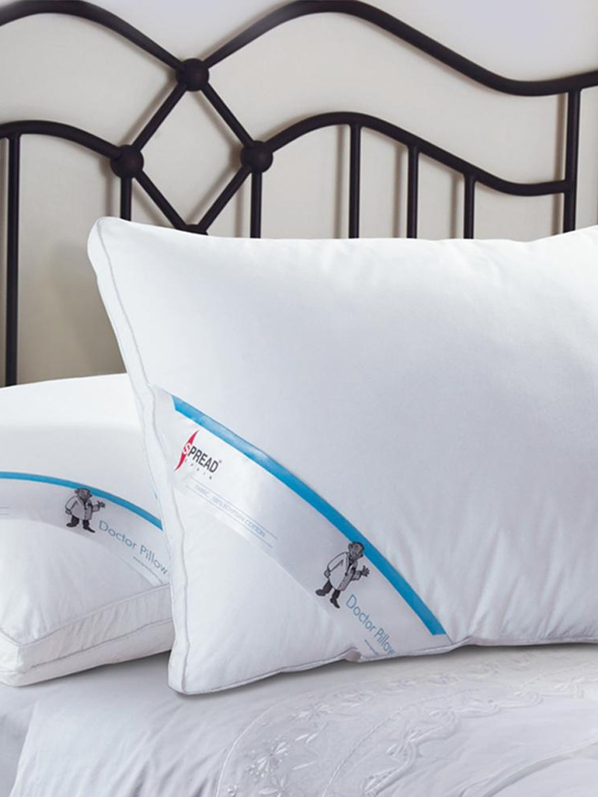 Two white Doctor Pillows with blue Spread branding on a metal framed bed