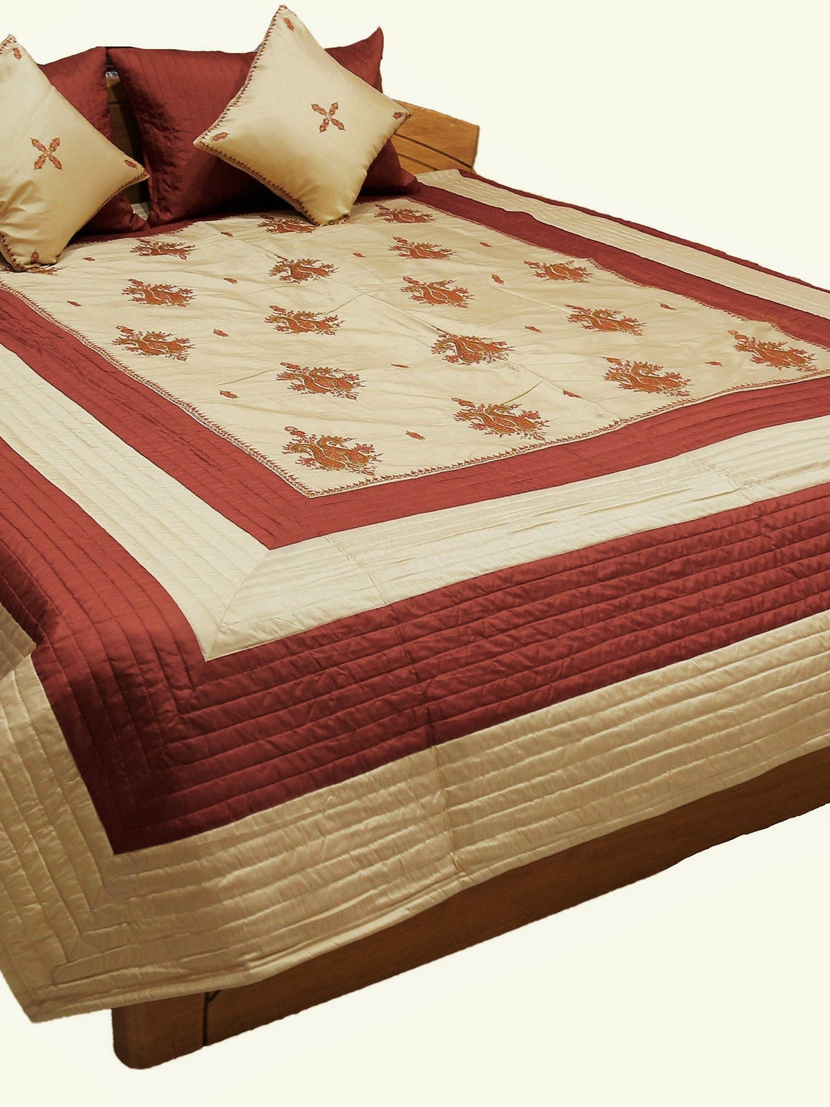 Maroon and cream double bedcover with a floral-embroidered border, styled with matching diamond-motif pillow covers