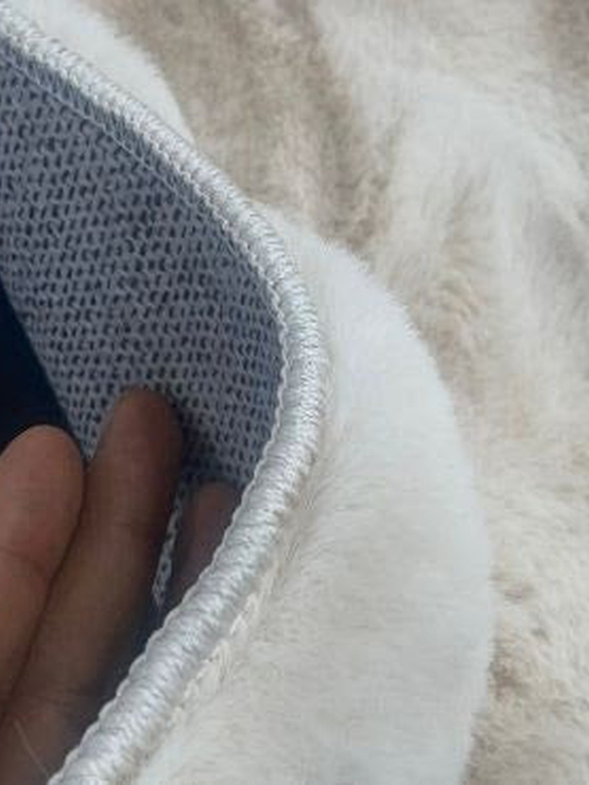 Corner of a cream faux fur mat lifted to show its grey non-slip backing