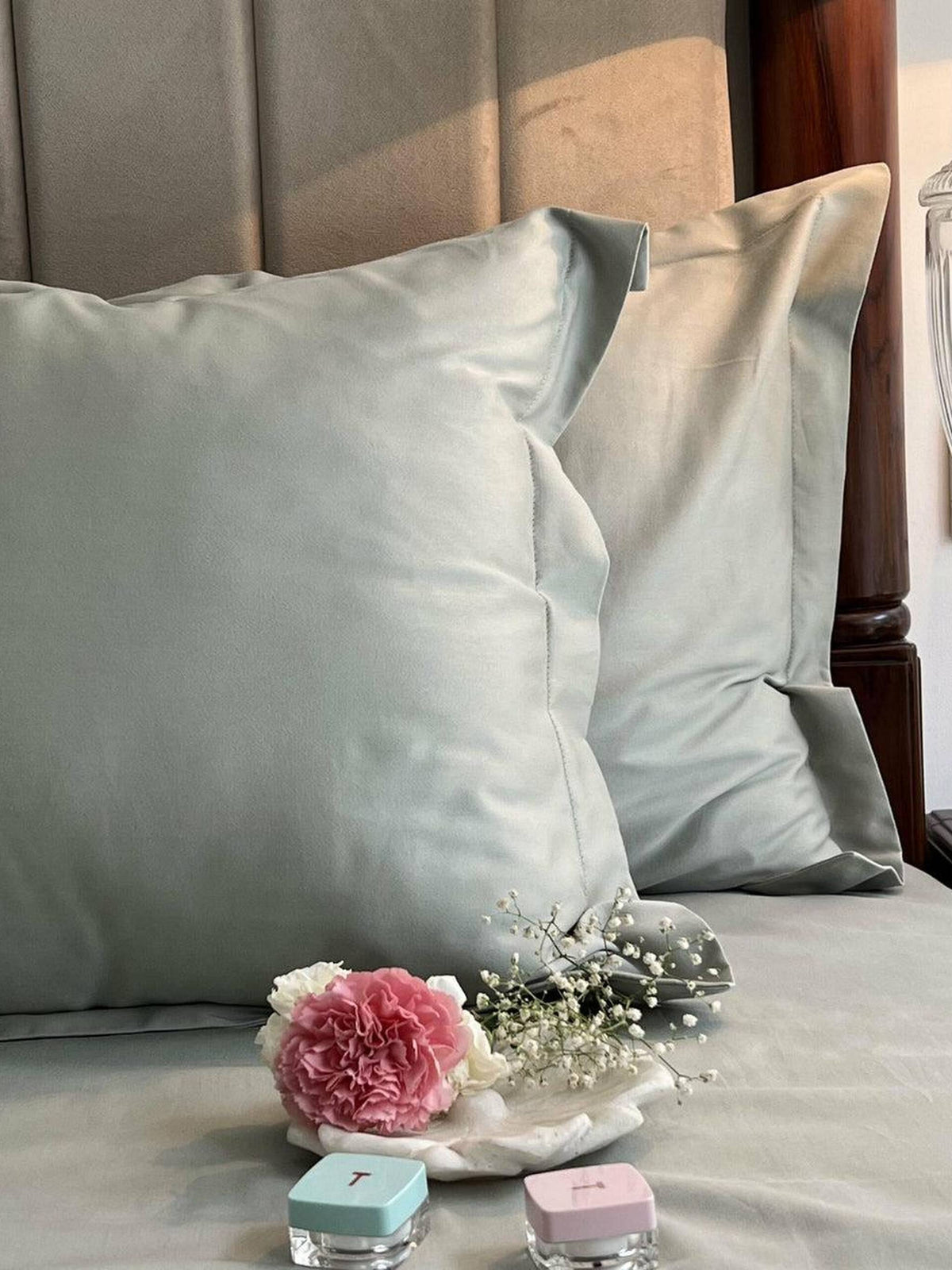 Sage green sateen pillows and bedding on a made bed