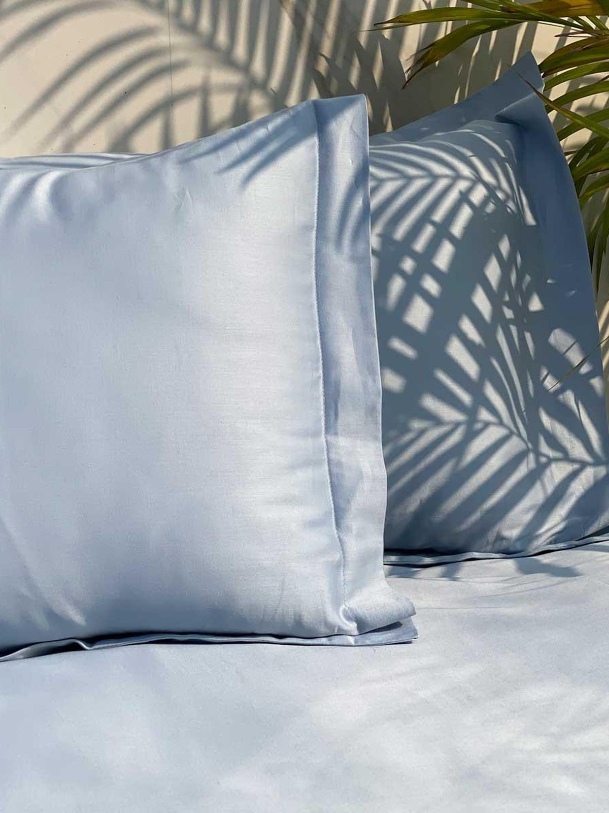 Smoke blue sateen pillows and bedding in sunlight with palm shadows