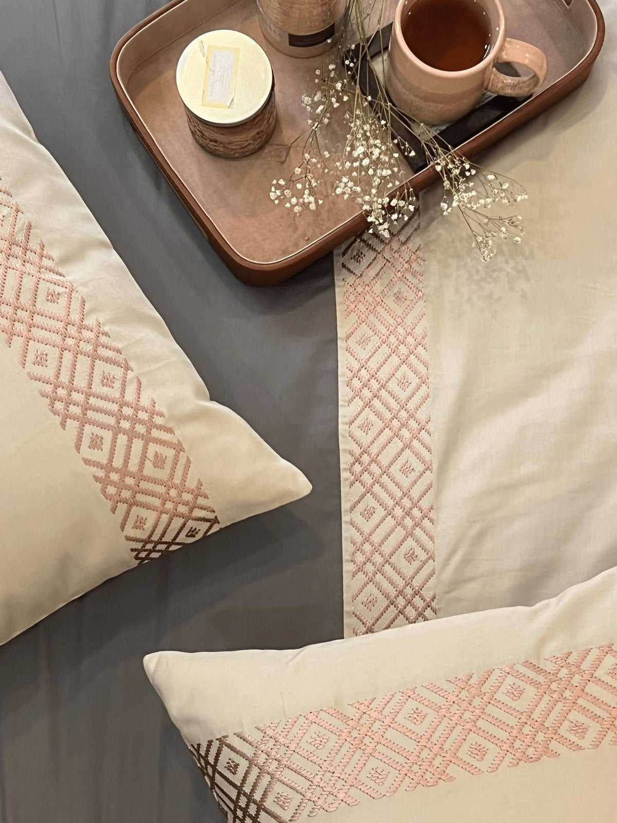 Cream pillows with a rose geometric embroidered band on charcoal sheets, Beige Classic