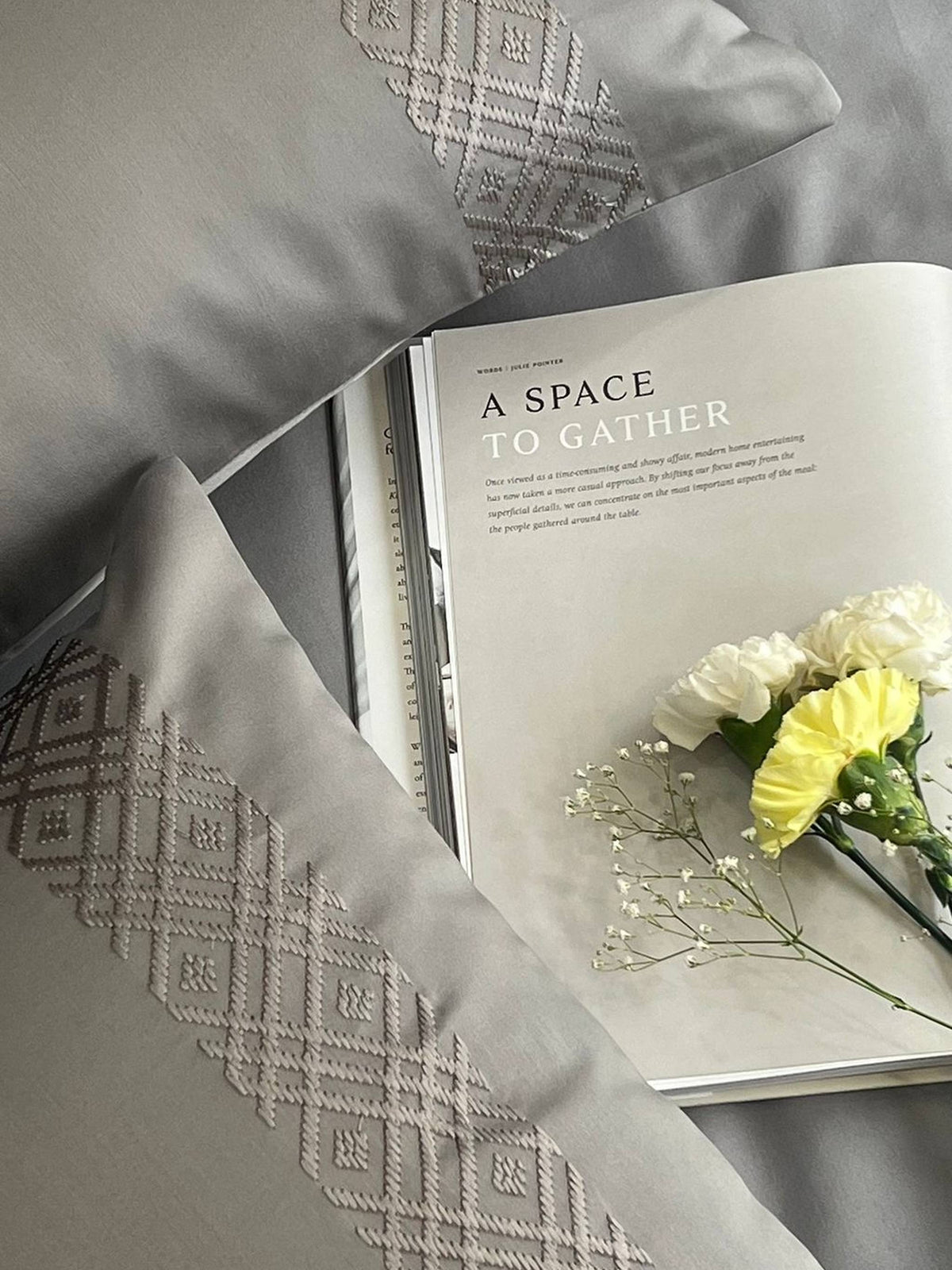 Silver grey pillow covers with a woven diamond band, magazine and yellow carnations