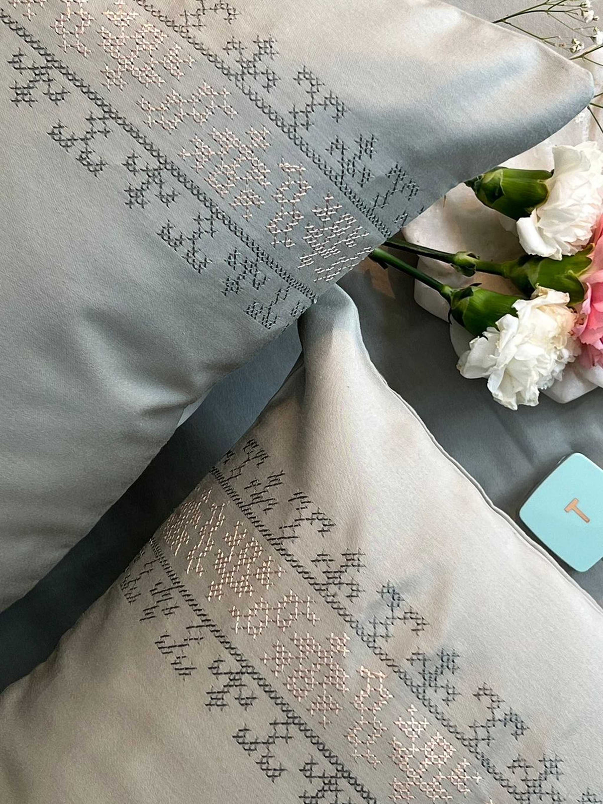 Sage green bedding with a grey and metallic cross-stitch embroidered band