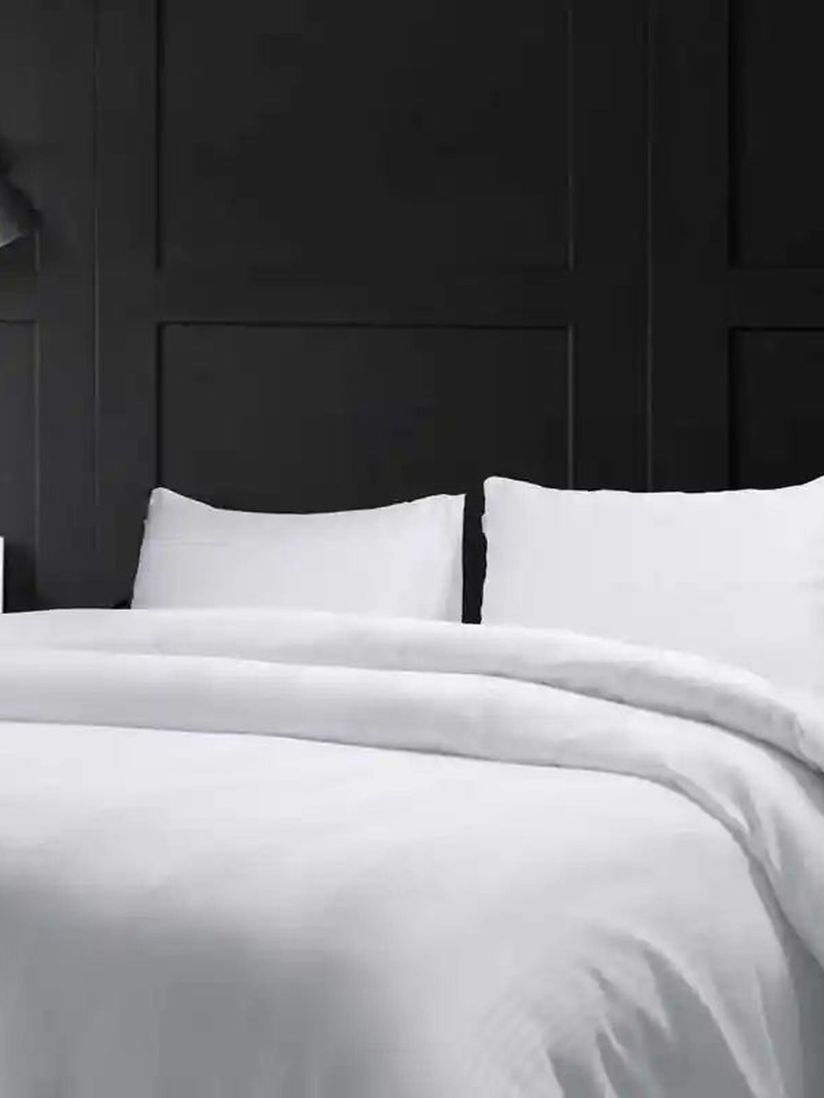 White cotton bedsheet and pillows on a made bed against dark panelling