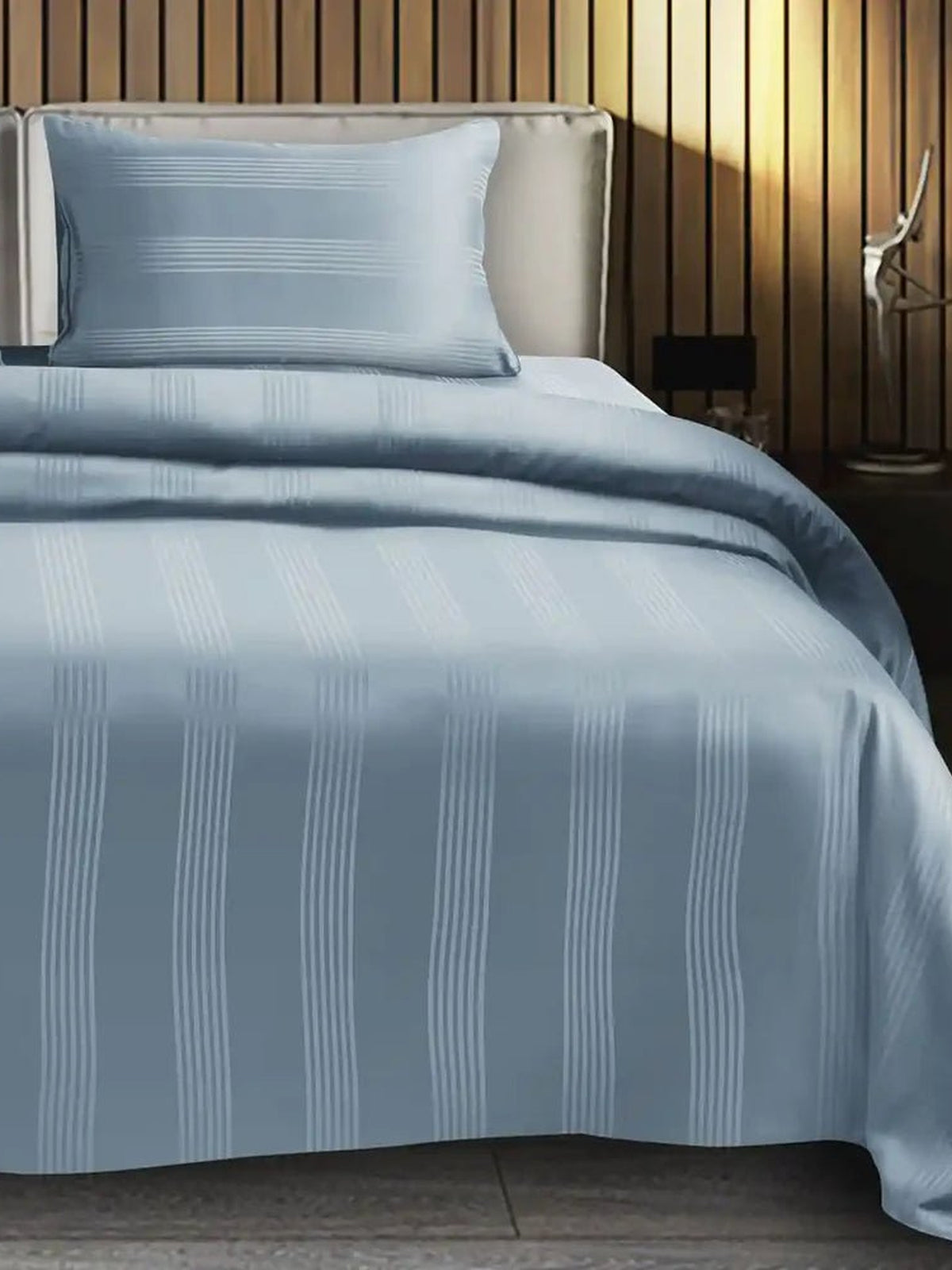 Pale blue grey satin stripe cotton bedsheet on a made bed with matching pillow