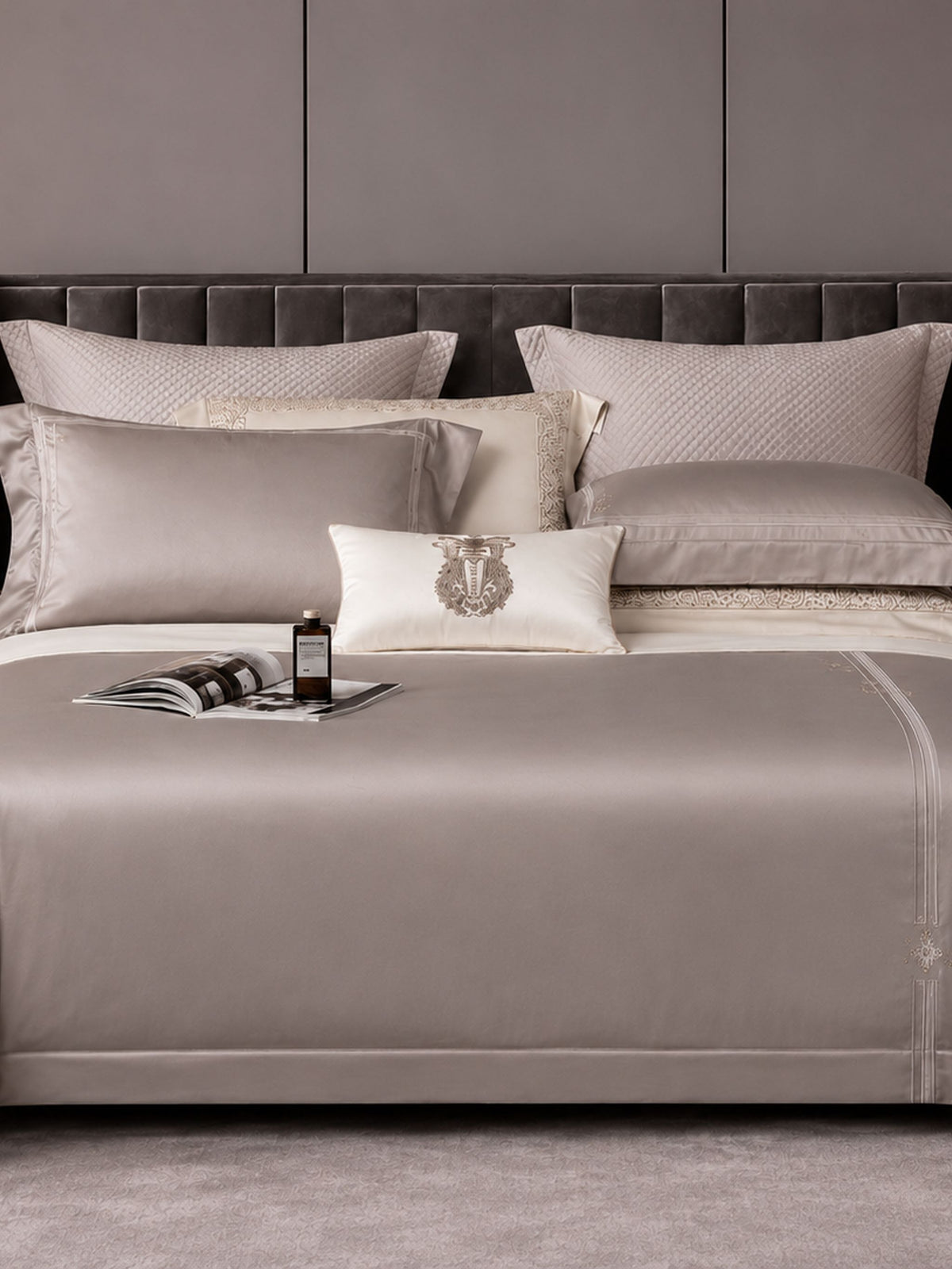 Taupe grey bedding with a fine embroidered border, made up on an upholstered bed