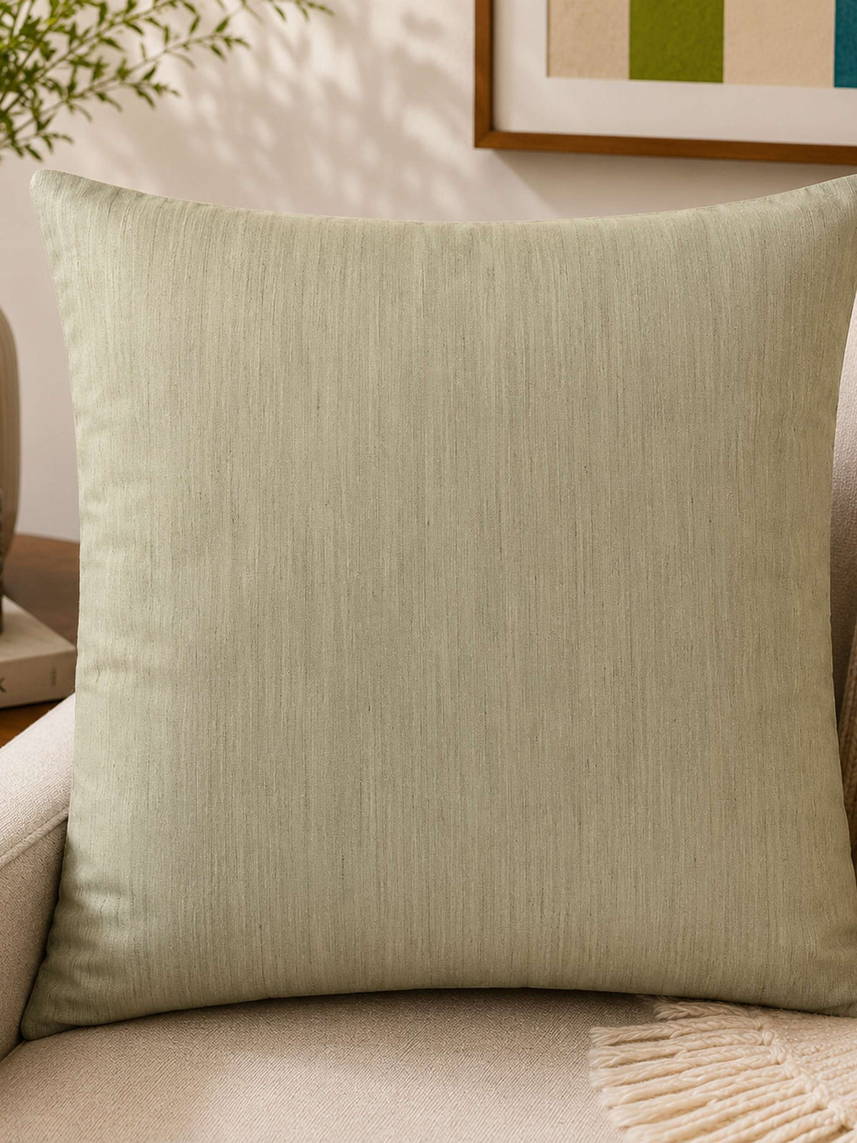 Pale sage-green plain cushion cover, shown staged on a sofa