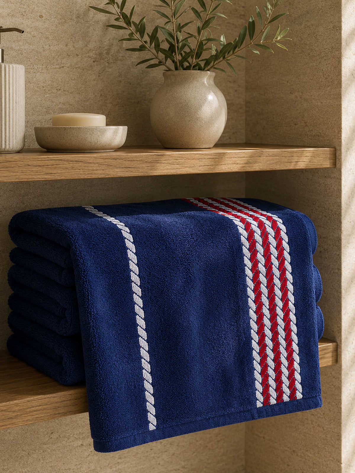 Navy cotton towels with a red and white braided stripe border, folded on a shelf