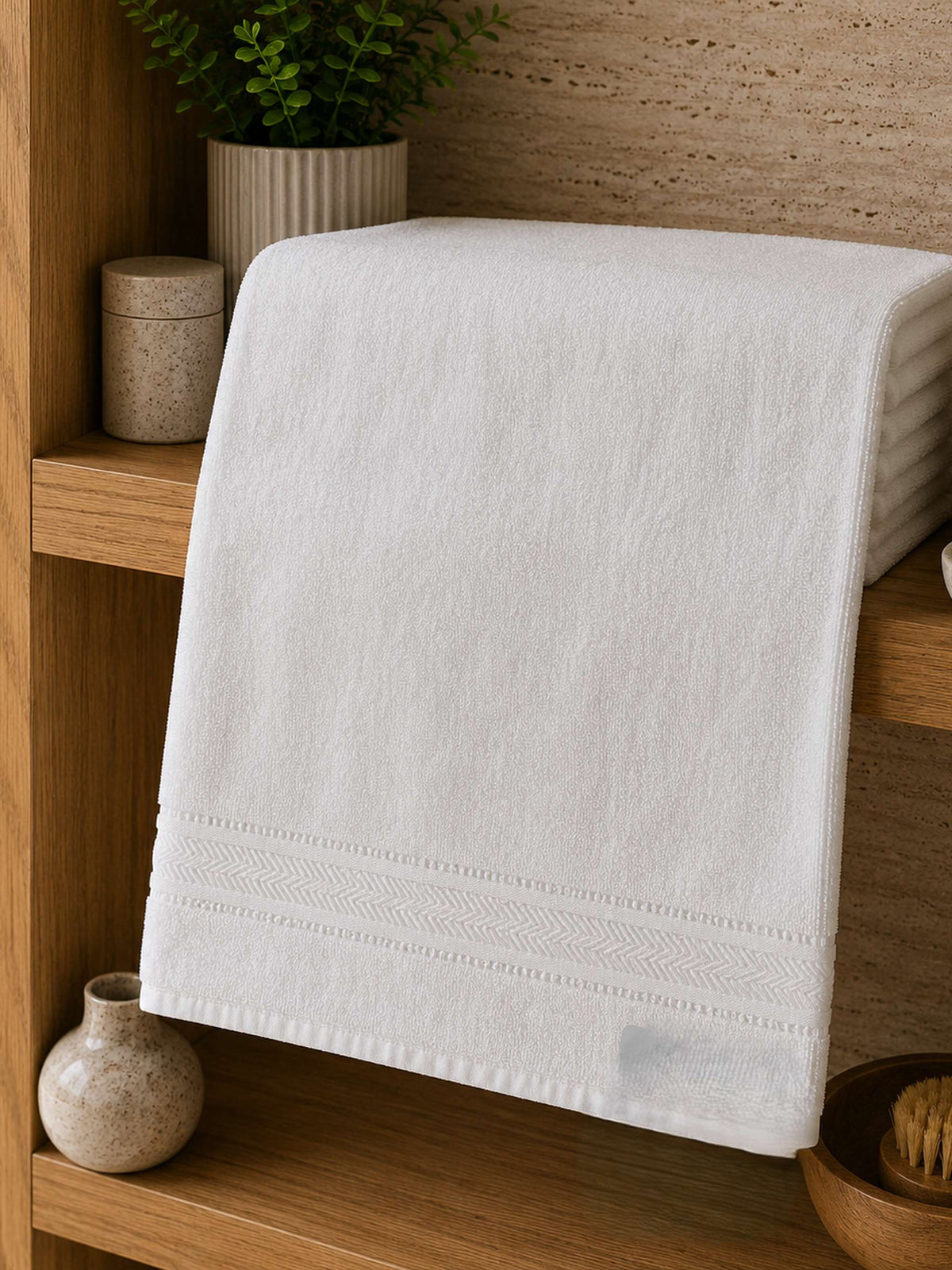 White cotton bath towel with woven border folded on a wooden bathroom shelf