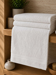 Ivory white cotton towels with a plain border, folded on a wooden shelf