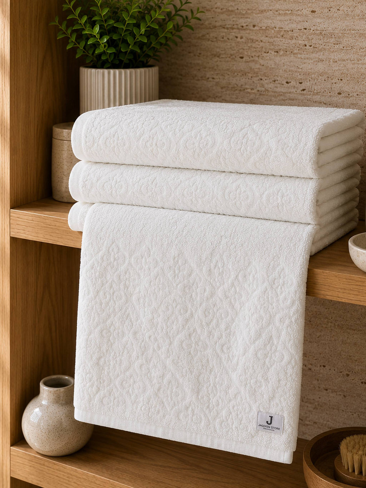 White cotton bath towel with an all-over floral damask pattern folded on a wooden bathroom shelf.