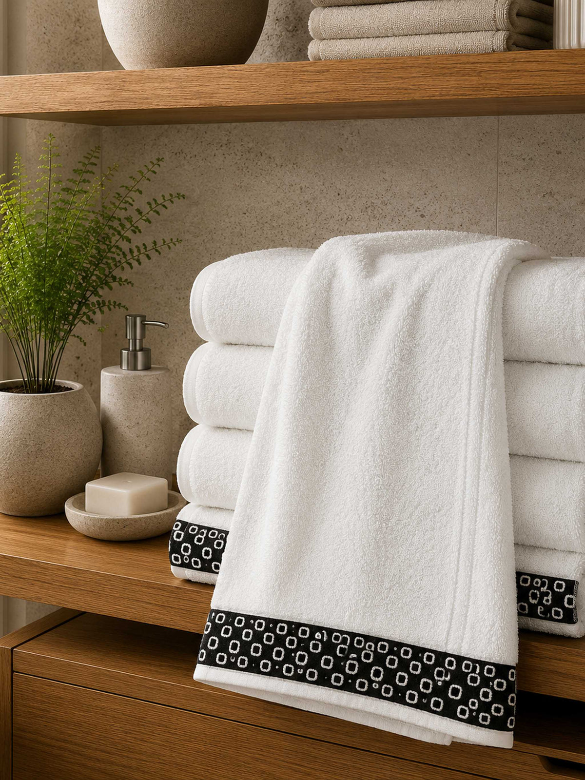 White cotton bath towel with black contrast woven border folded on a wooden bathroom shelf