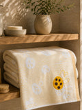 Yellow printed cotton bath towel with bee design folded on a wooden bathroom shelf