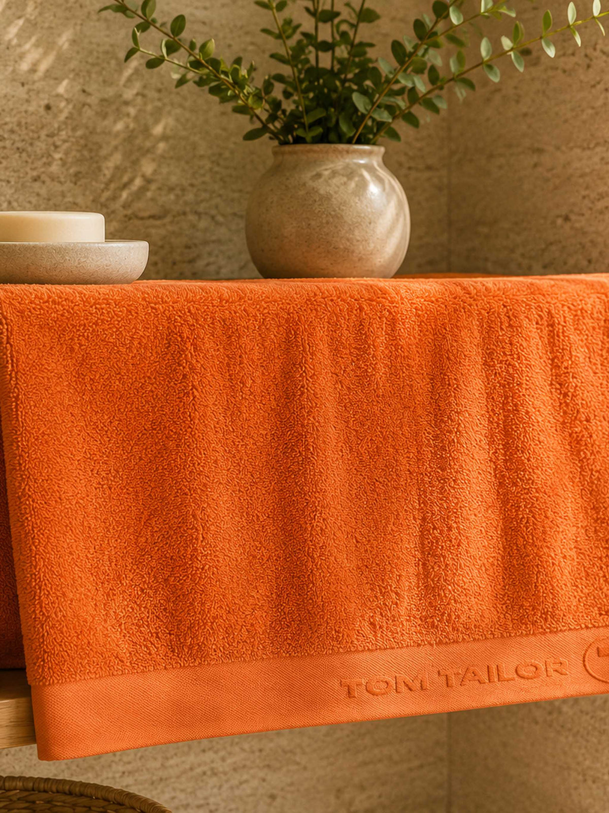 Orange cotton bath towel with woven border placed in a  modern bathroom