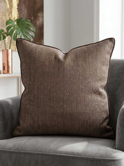 Textured brown woven cushion cover with piped edge on a grey armchair
