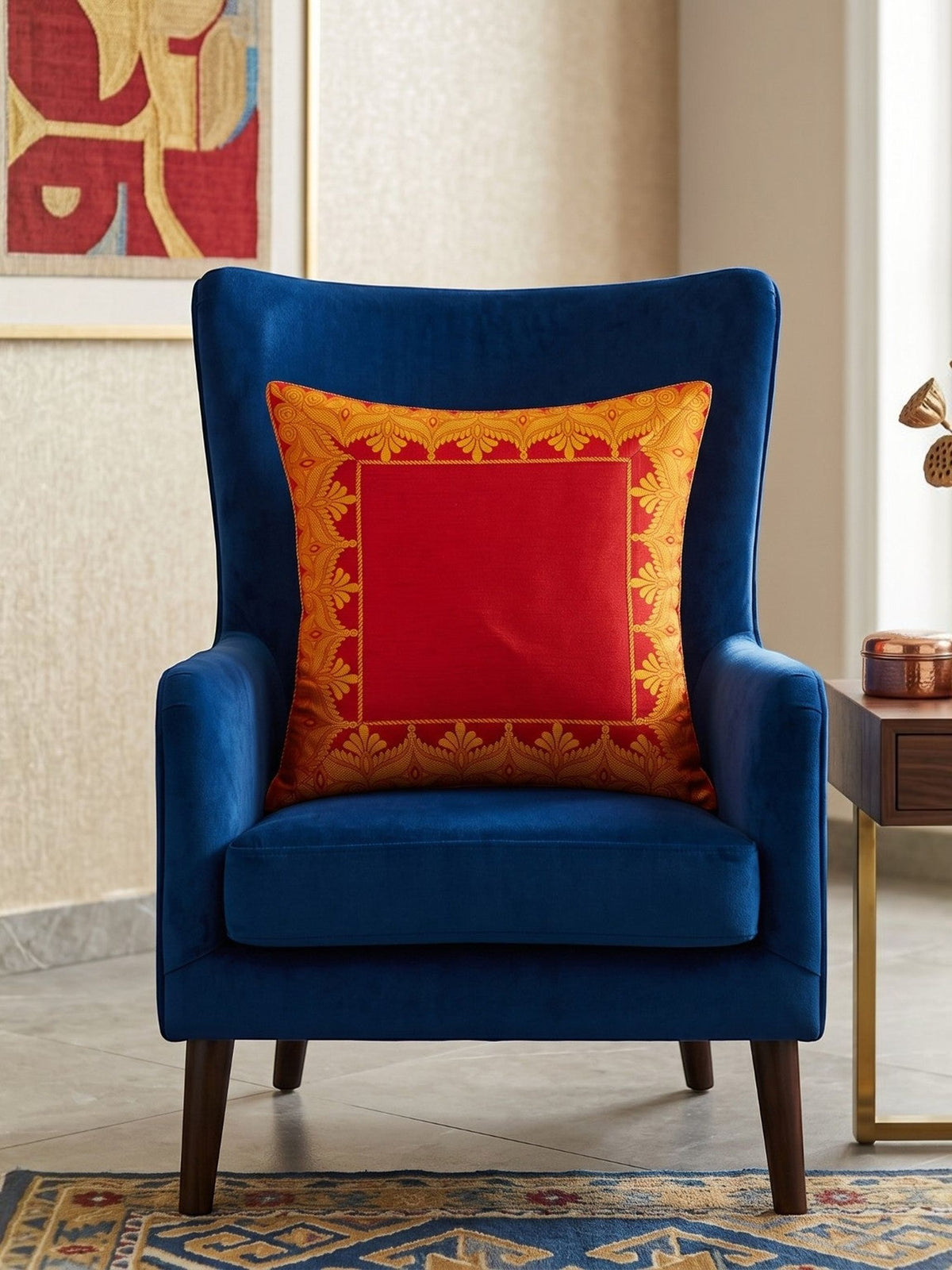 Red embroidered polysilk cushion cover with golden ornamental border design on a blue accent chair