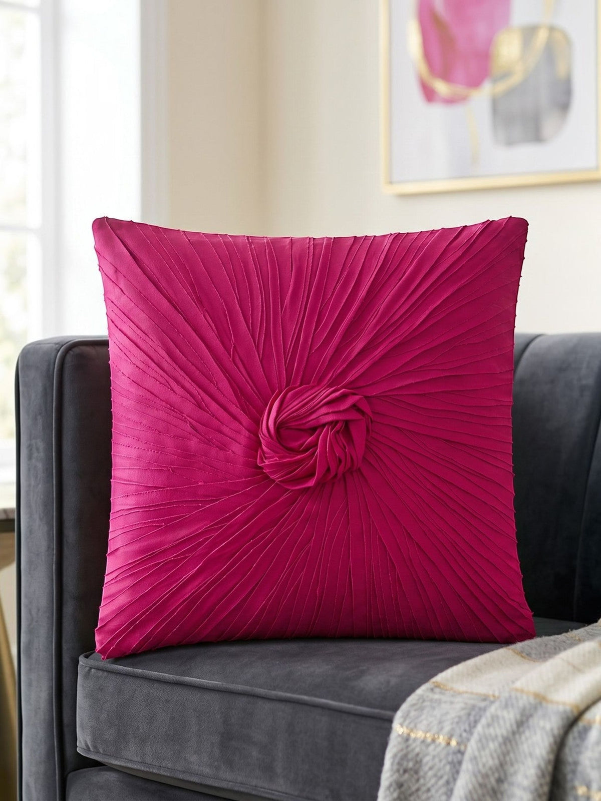 Pink pleated pillow on a gray couch with a gold side table and abstract art in the background.