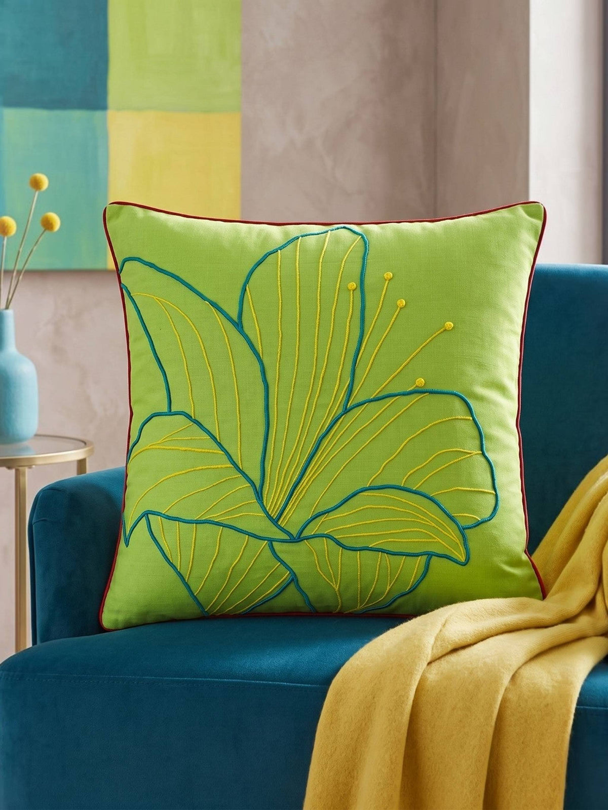 Lime green cushion cover with a teal outline leaf embroidery on a blue armchair