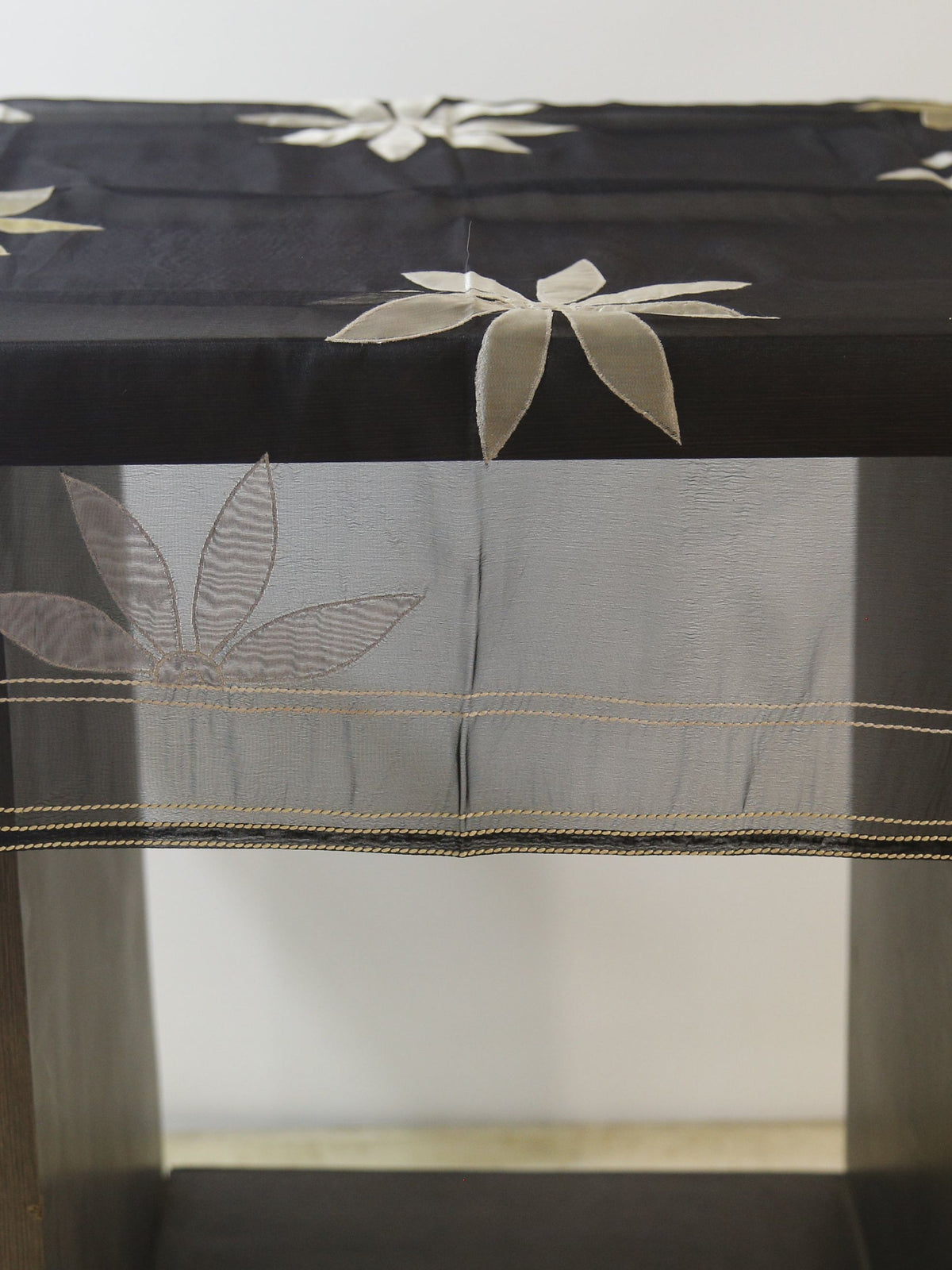 Black sheer organza table cover with a scattered cream appliqué flower pattern and a woven-stripe sheer border, draped over a small display table