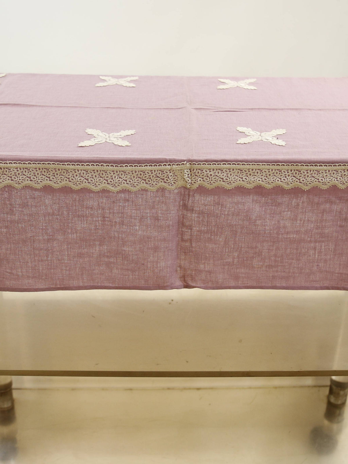 Solid lavender linen table cover with small white embroidered cross motifs and a white crochet lace border