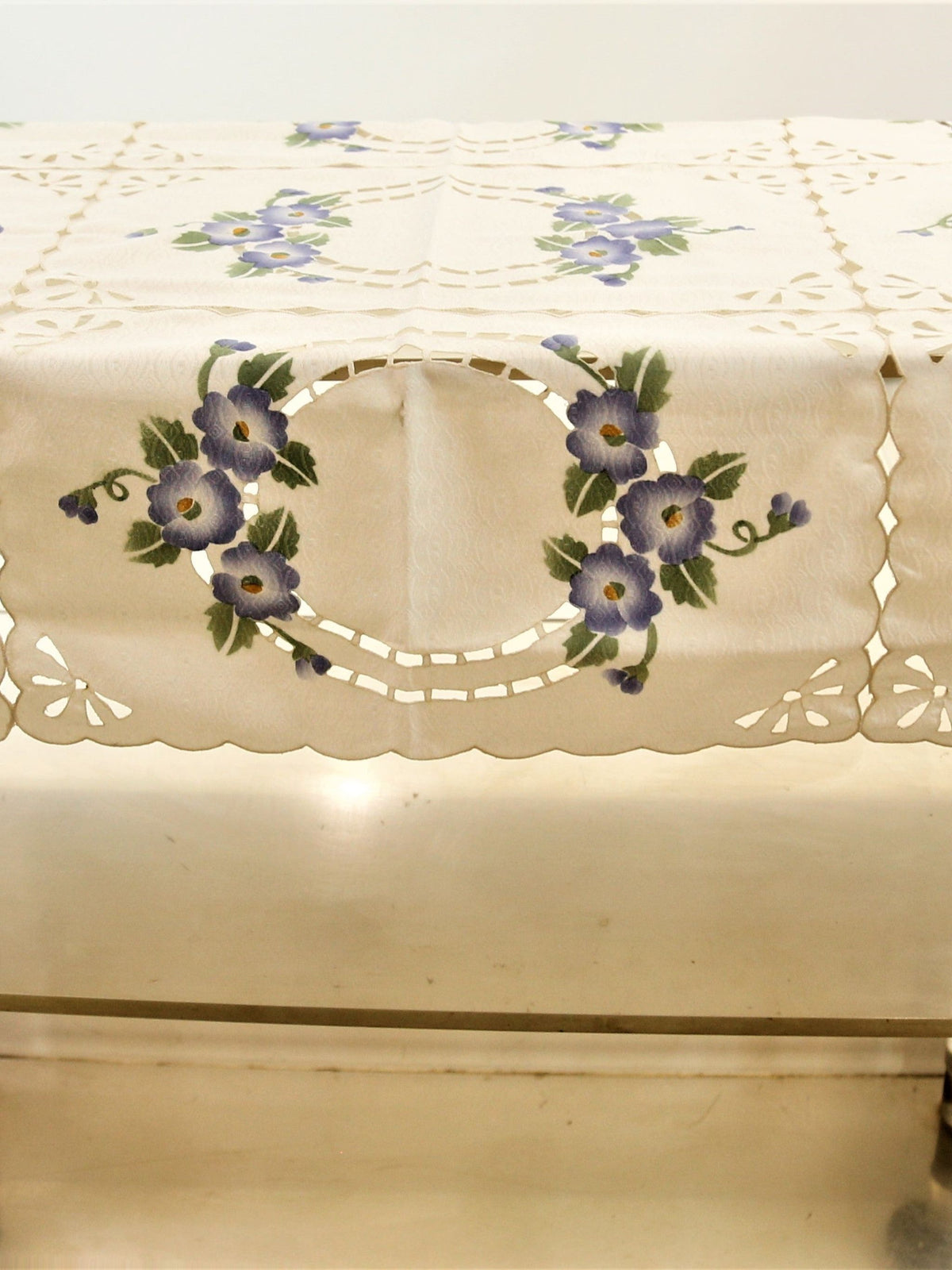 Cream table cover with a cutwork lattice pattern, printed purple-blue floral bouquets, and a scalloped cutwork hem
