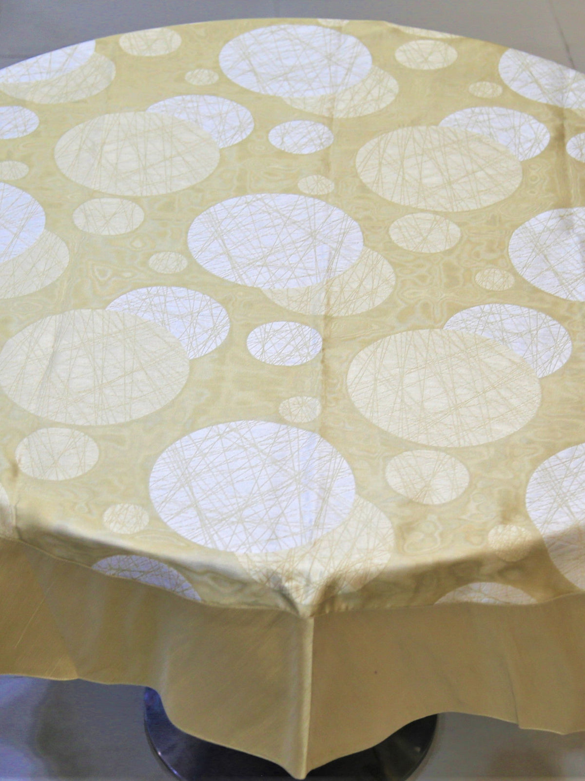Round pale gold table cover with a white circular thread-art bubble print