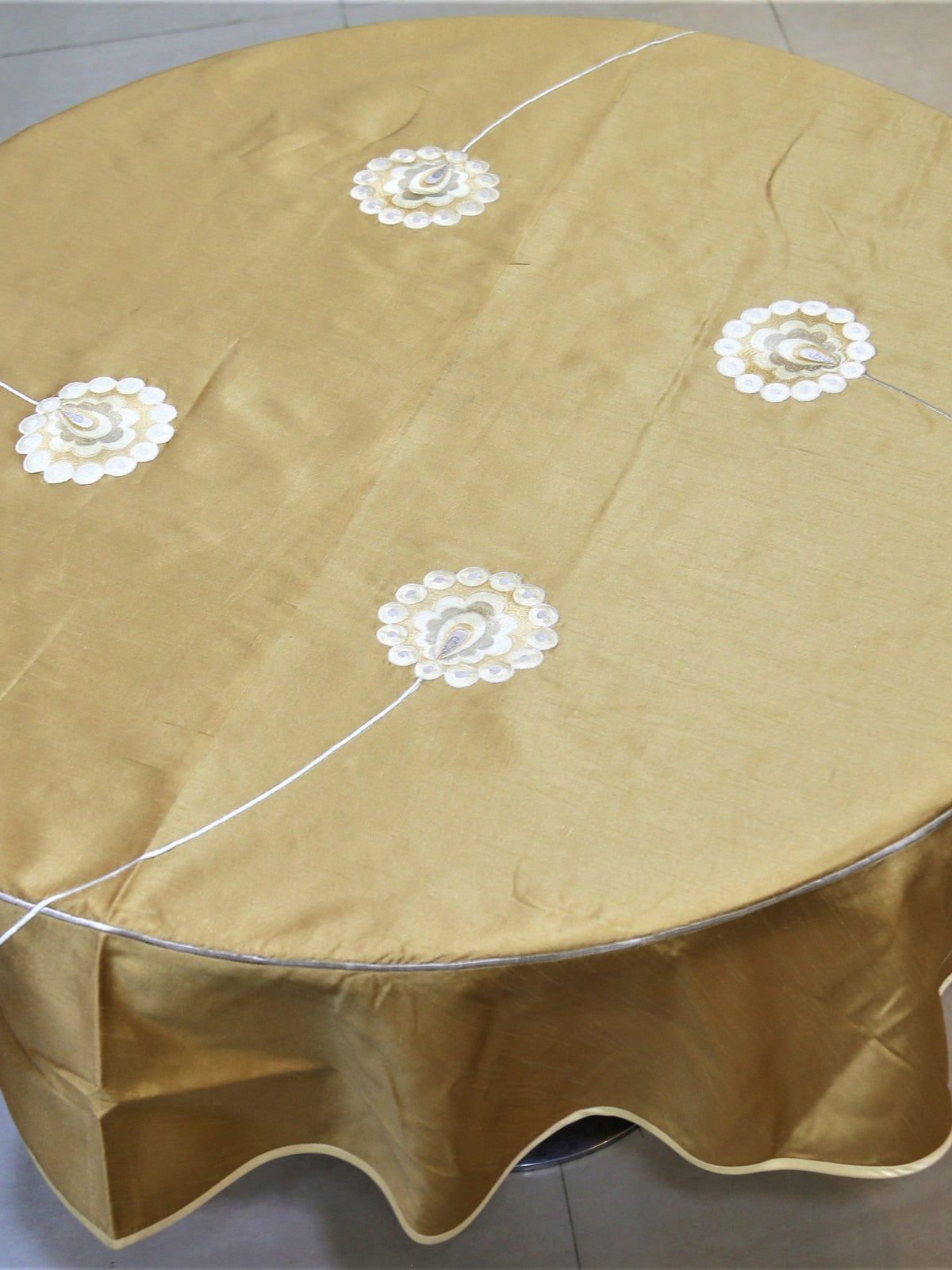 Round solid gold table cover with scattered white flower appliqués and a scalloped hem