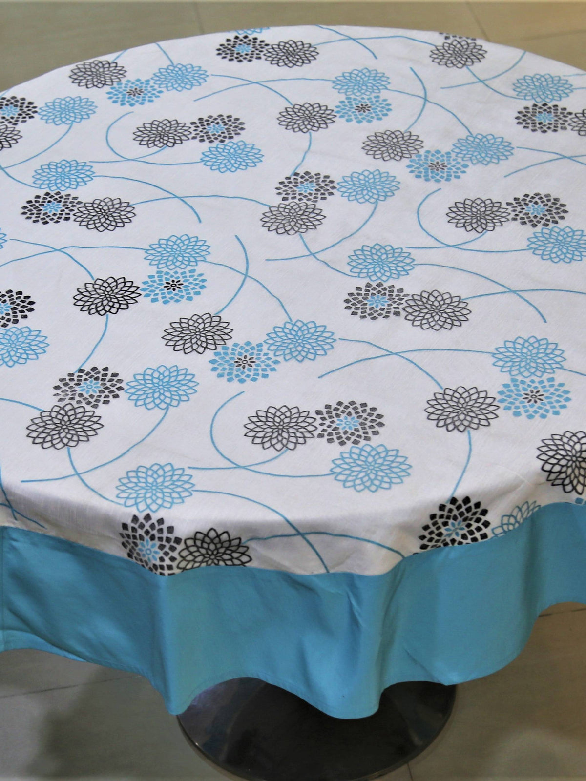 Round white table cover with a black and blue floral burst print and a solid sky-blue underskirt