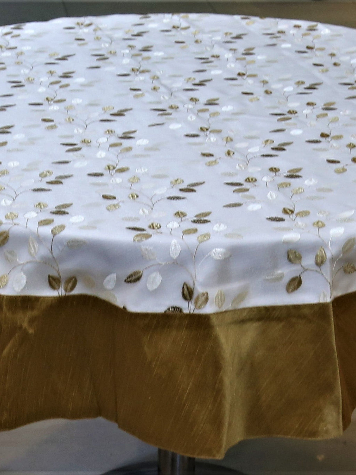 Round cream table cover with a gold-brown embroidered leaf-vine pattern and a matching gold-brown underskirt